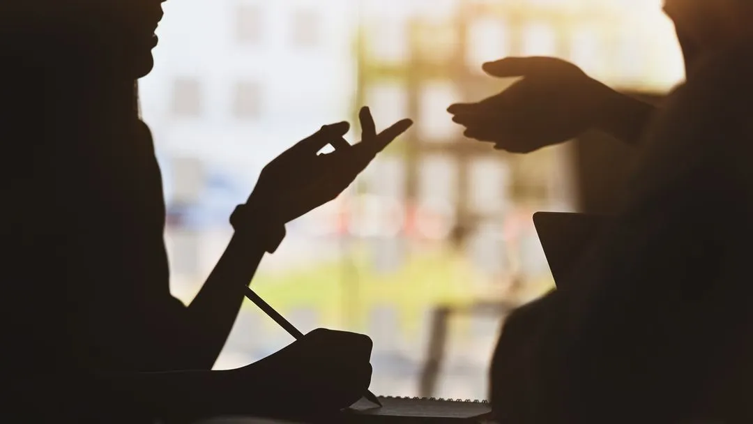 Silhouette von 2 Personen mit Notebook in der Hand während eines Gesprächs